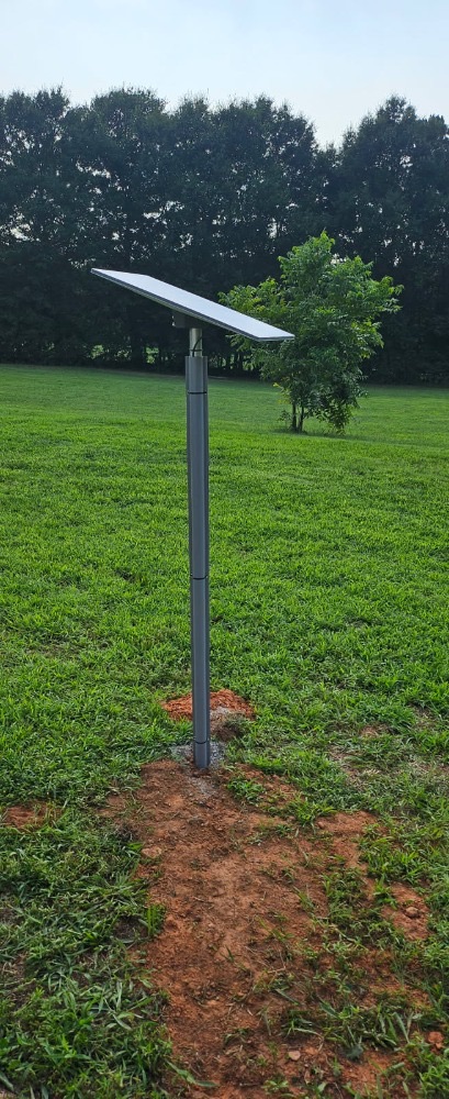 Starlink dish on a steel pole mount standing in an open field with a clear view of the sky